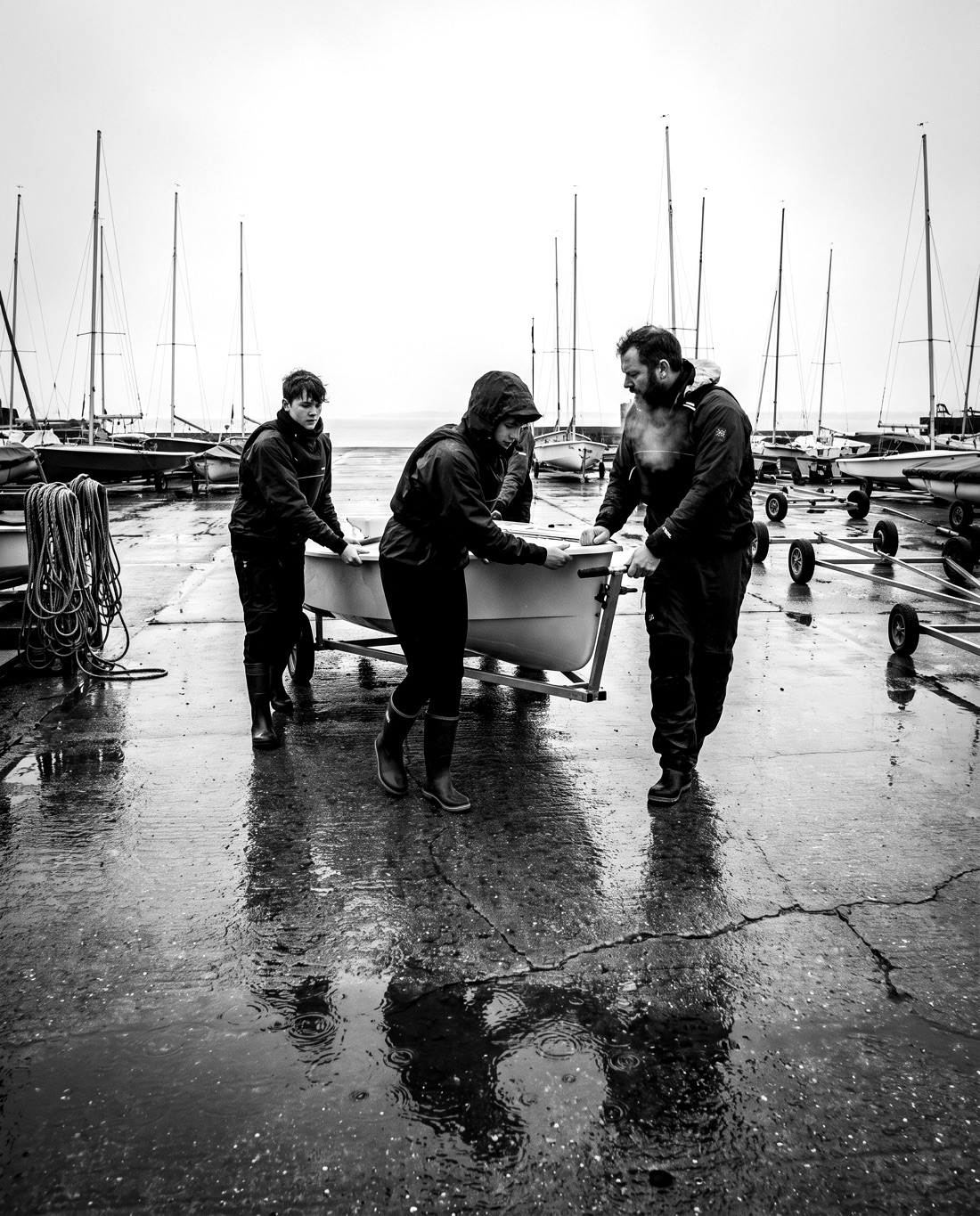 Sailors and a coach pushing a dinghy up a wet slipway at dawn