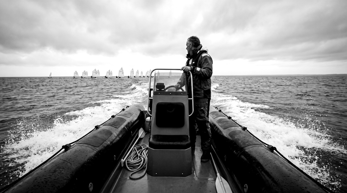 A coach at the wheel of a rib, watching the fleet race