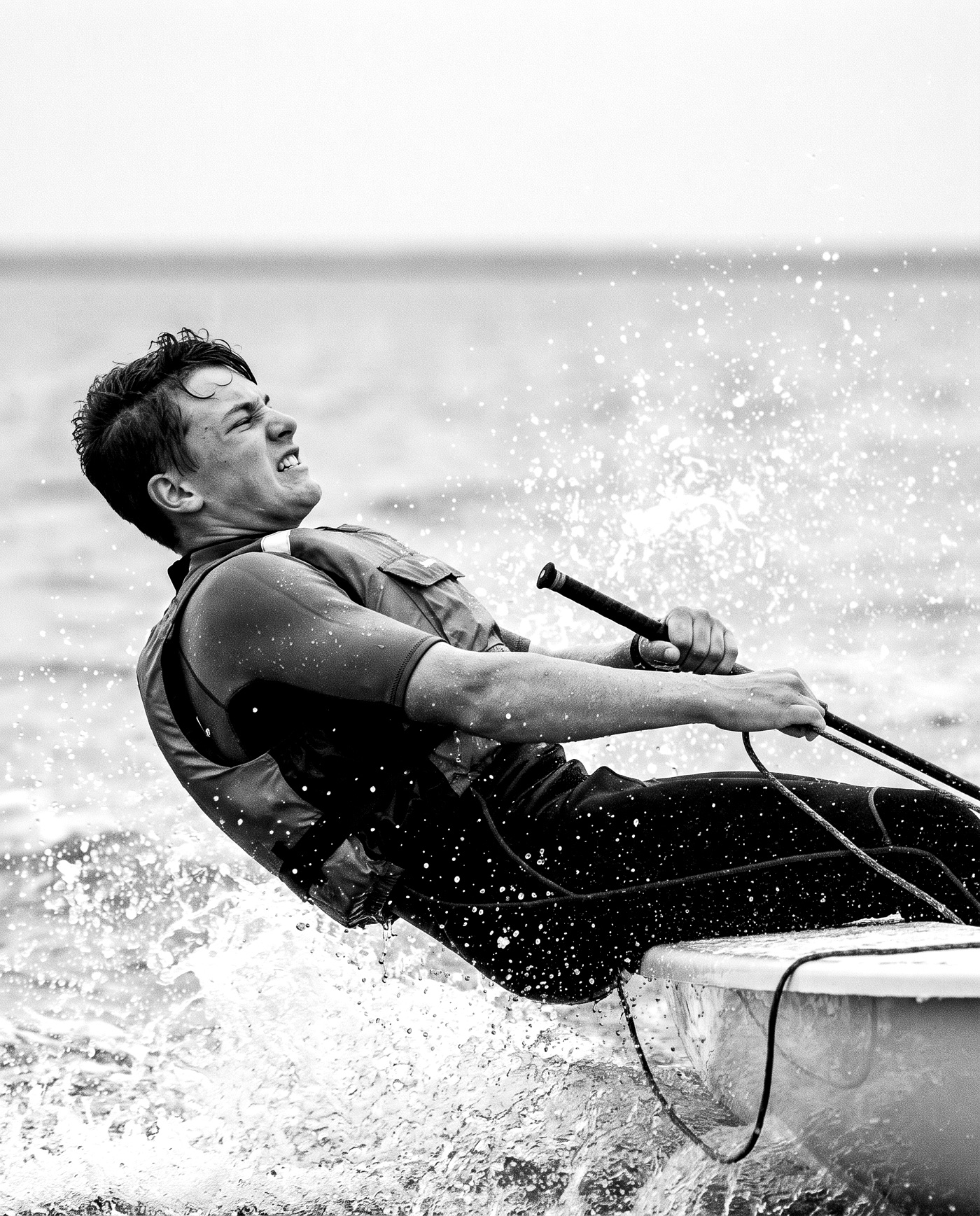 A sailor hiking flat out over the side as spray bursts across the frame